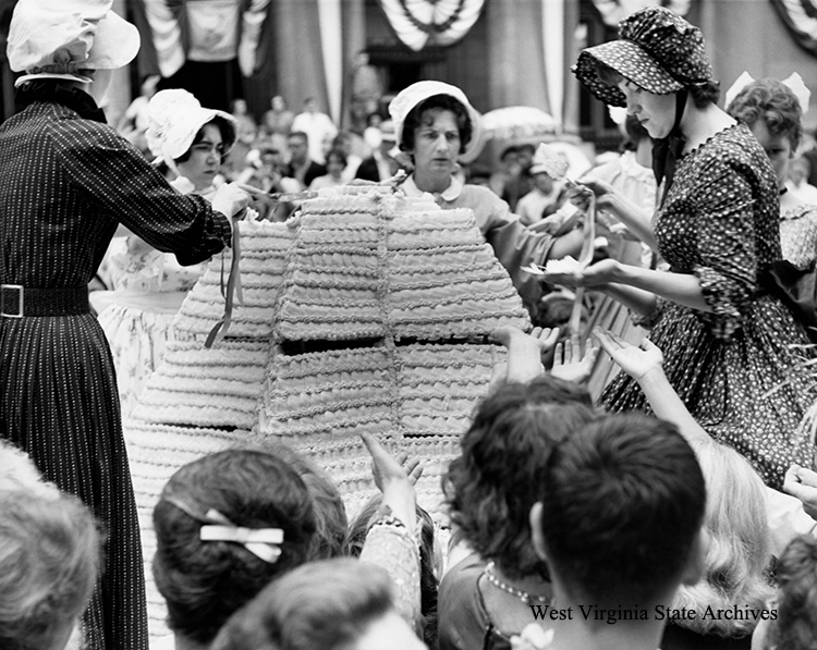 Women wearing bonnets serving the 35-layer, 750 pound birthday cake in middle of Capitol Street, Charleston, on Statehood Day, June 20, 1963. Archives Collection, West Virginia State Archives (343911)